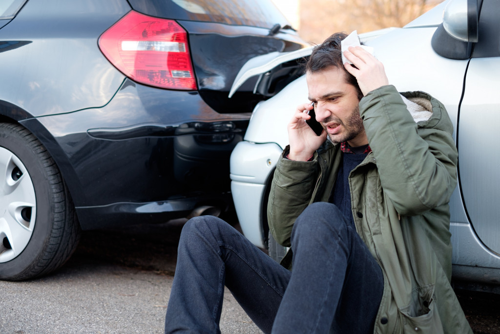 Man seated beside his car because of an accident while calling someone