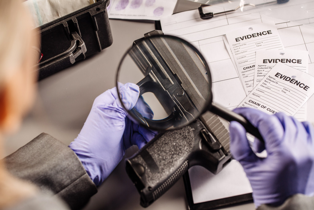 A person inspecting a gun as evidence using a magnifying glass