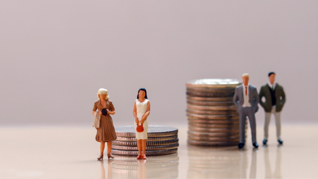 Miniature men and women standing beside stacks of coins symbolizing pay gap