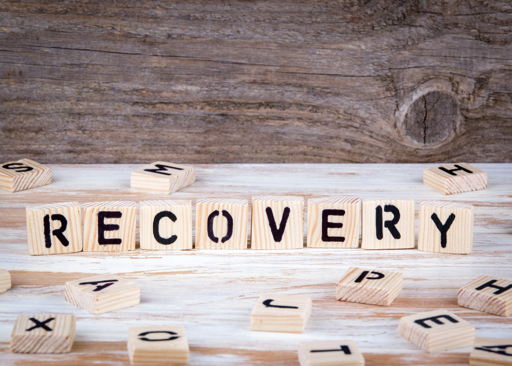 The word recovery spelled out on a wooden background using Scrabble tiles.